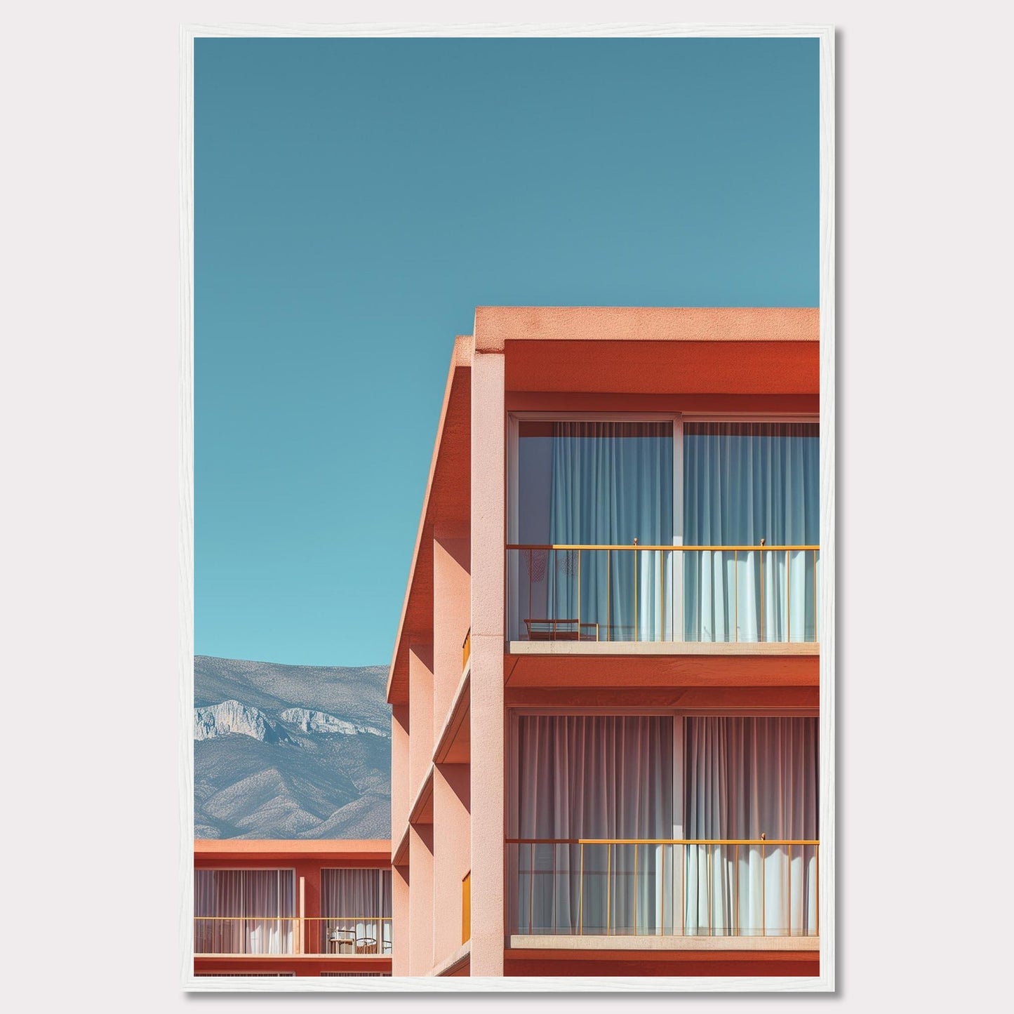 This captivating image showcases a modern building with a vibrant orange facade under a clear blue sky. The structure features large glass windows with white curtains, and balconies equipped with minimalistic furniture. In the background, majestic mountains add a serene touch to the scene.