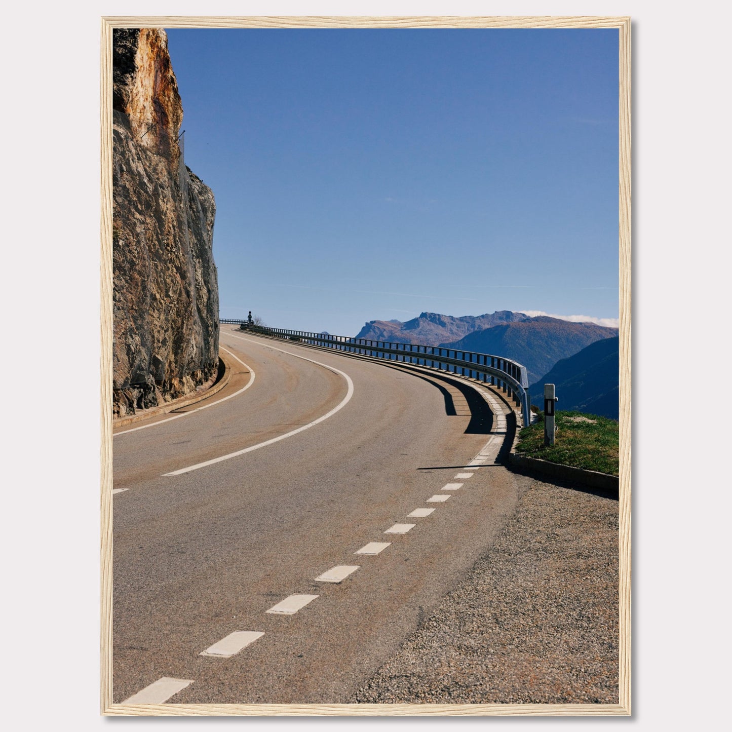 This captivating photograph showcases a winding mountain road bordered by a sheer rock face on one side and a protective guardrail on the other. The clear blue sky and distant mountain range add to the scene's serene beauty.v