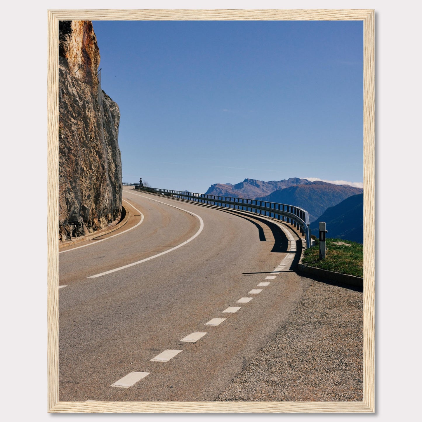 This captivating photograph showcases a winding mountain road bordered by a sheer rock face on one side and a protective guardrail on the other. The clear blue sky and distant mountain range add to the scene's serene beauty.