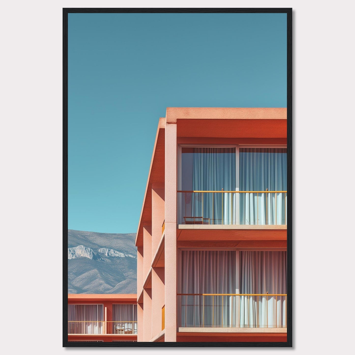 This captivating image showcases a modern building with a vibrant orange facade under a clear blue sky. The structure features large glass windows with white curtains, and balconies equipped with minimalistic furniture. In the background, majestic mountains add a serene touch to the scene.