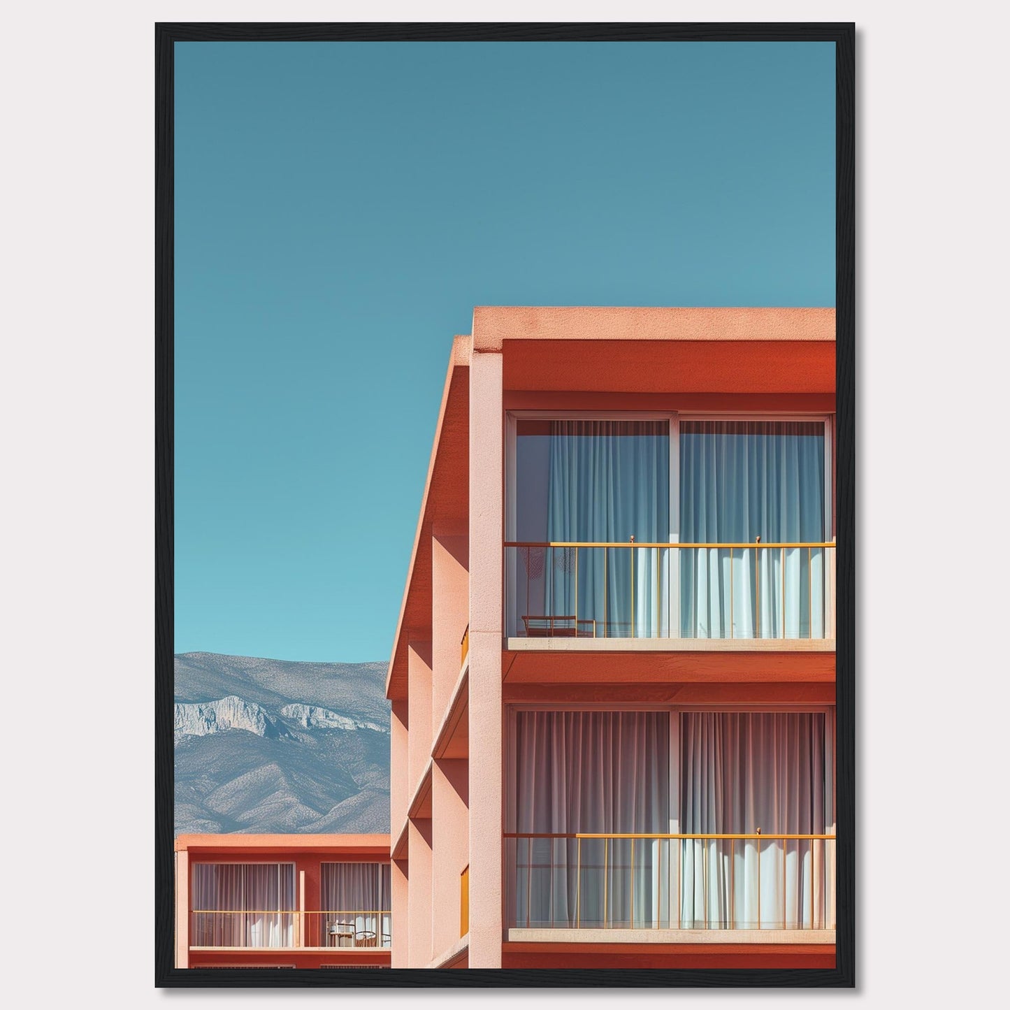 This captivating image showcases a modern building with a vibrant orange facade under a clear blue sky. The structure features large glass windows with white curtains, and balconies equipped with minimalistic furniture. In the background, majestic mountains add a serene touch to the scene.