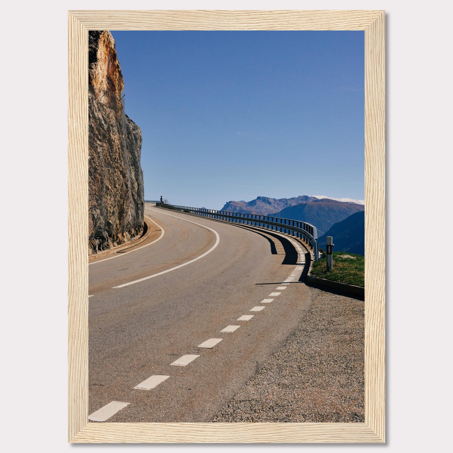 This captivating photograph showcases a winding mountain road bordered by a sheer rock face on one side and a protective guardrail on the other. The clear blue sky and distant mountain range add to the scene's serene beauty.