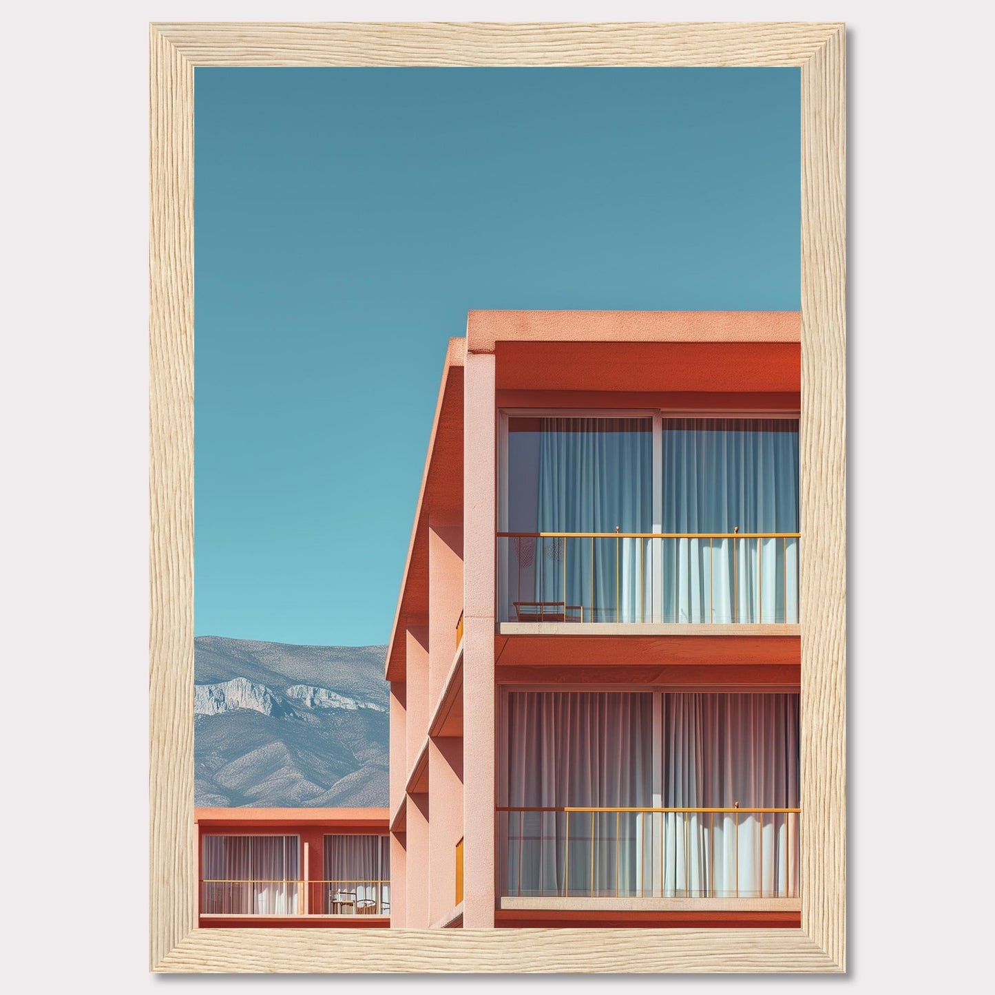 This captivating image showcases a modern building with a vibrant orange facade under a clear blue sky. The structure features large glass windows with white curtains, and balconies equipped with minimalistic furniture. In the background, majestic mountains add a serene touch to the scene.