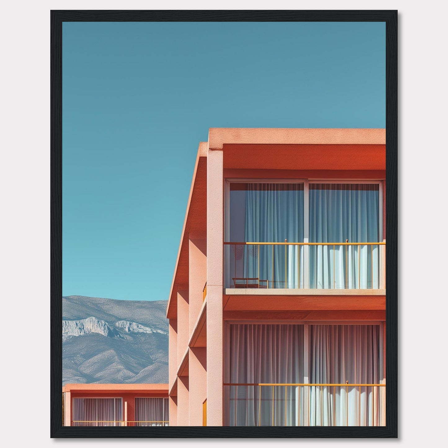 This captivating image showcases a modern building with a vibrant orange facade under a clear blue sky. The structure features large glass windows with white curtains, and balconies equipped with minimalistic furniture. In the background, majestic mountains add a serene touch to the scene.