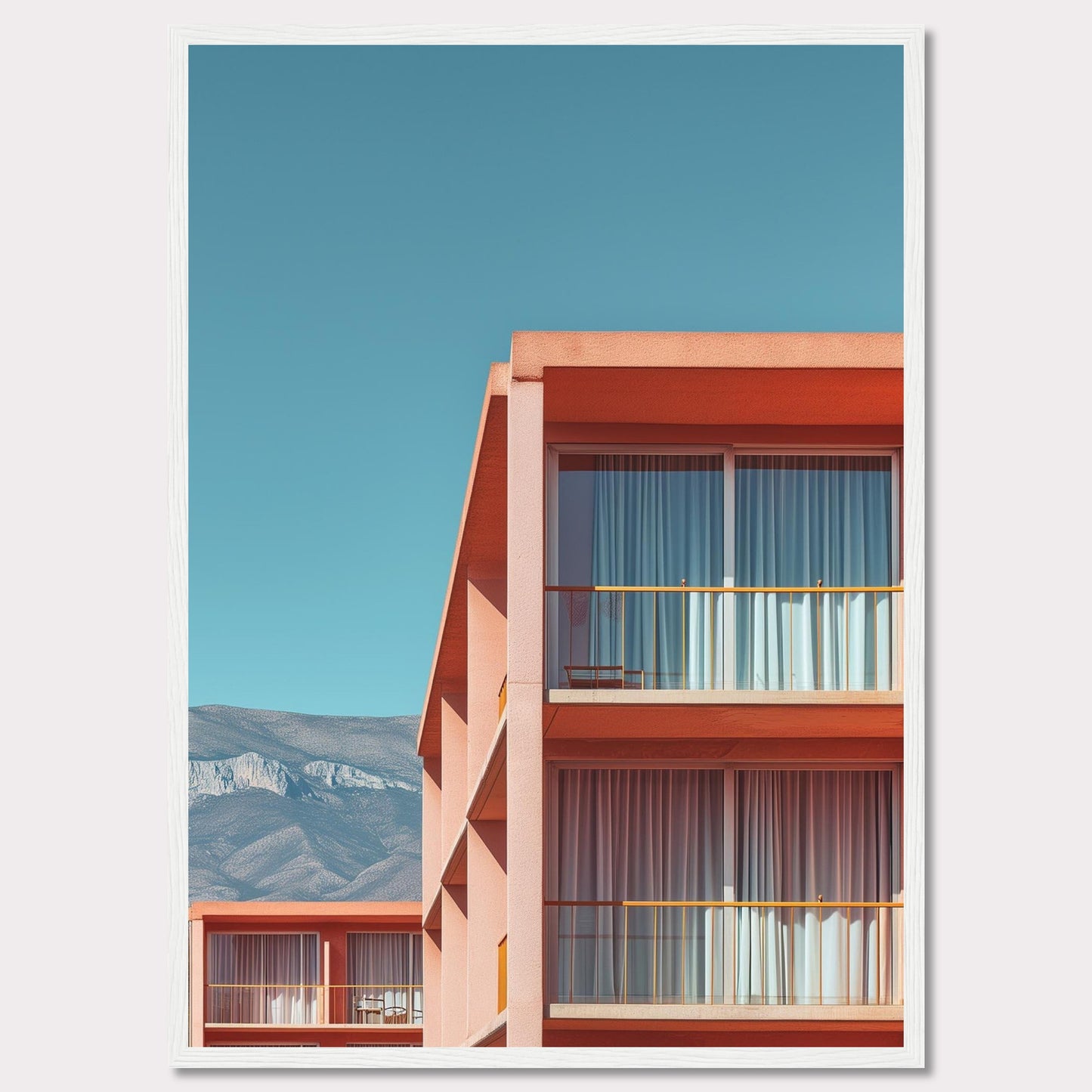 This captivating image showcases a modern building with a vibrant orange facade under a clear blue sky. The structure features large glass windows with white curtains, and balconies equipped with minimalistic furniture. In the background, majestic mountains add a serene touch to the scene.